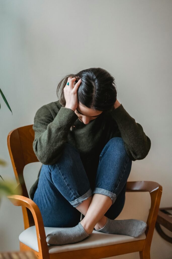 Chica triste sentada en una silla sujetándose la cabeza.